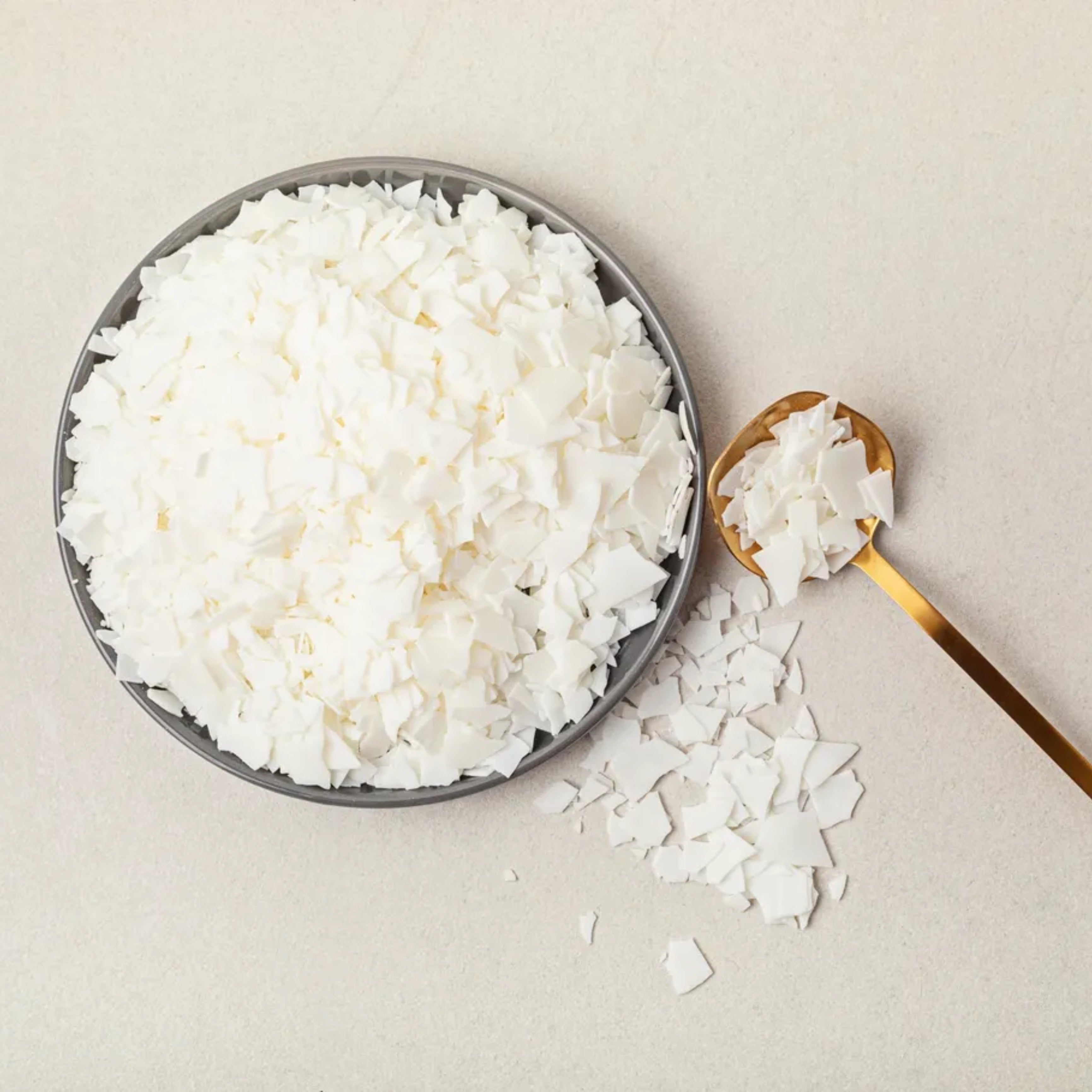 White candle wax flakes in a bowl with a scoop of wax to the right.